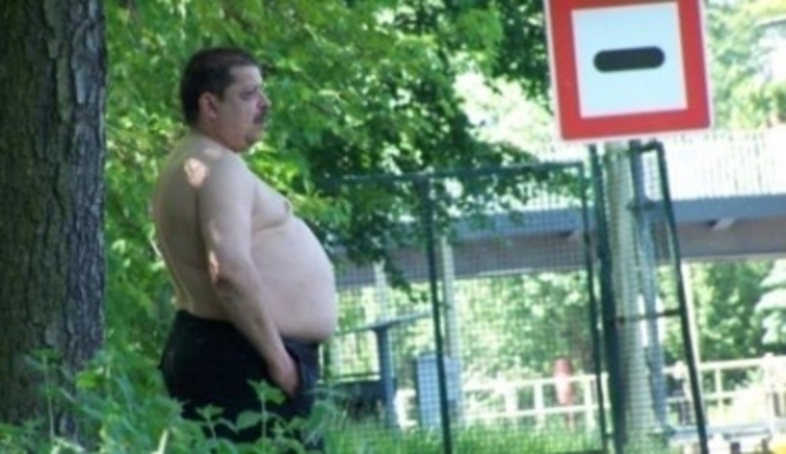 Obézní člověk bez trička stojící na zastávce veřejné hromadné dopravy