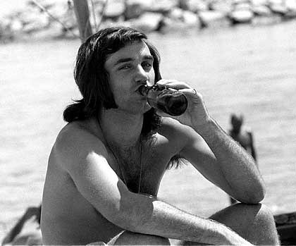 Muž sedící na pláží s láhví v ruce