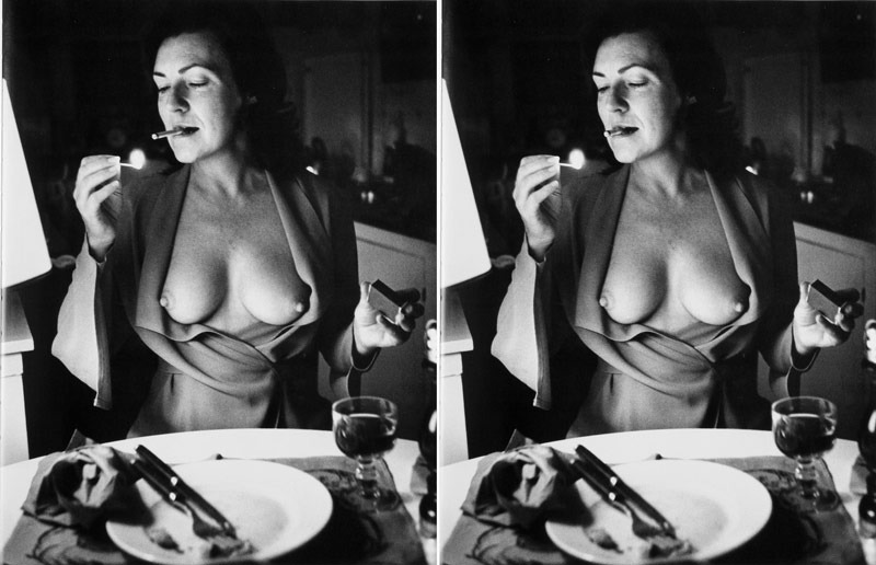 Žena sedící u stolu s odhalenými prsy si zapaluje cigaretu
