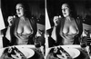 Žena sedící u stolu s odhalenými prsy si zapaluje cigaretu