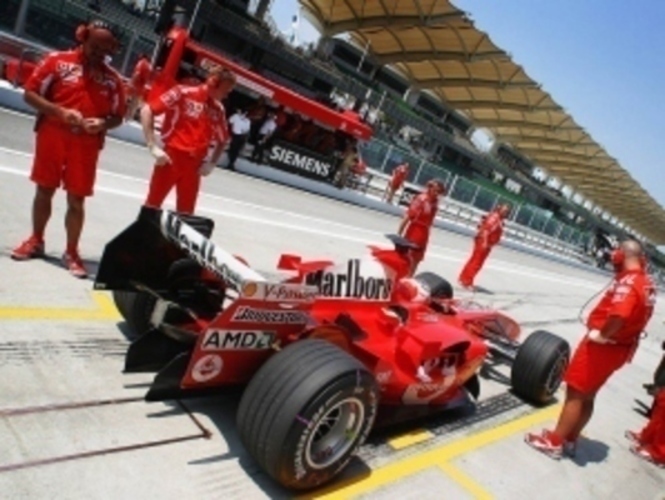 Pohled na zadní křídlo formule 1 automobilu značky Ferrari stojící s mechaniky v depu