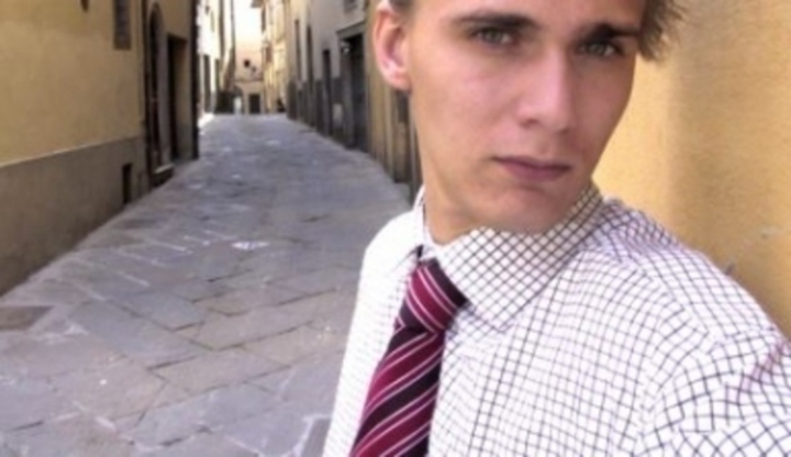 Muž stojící v uličce oblečen do pánské košile s kravatou a je opřen o zeď