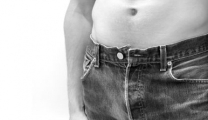 Černobílý snímek zachycující nahé mužské břicho v džínách
