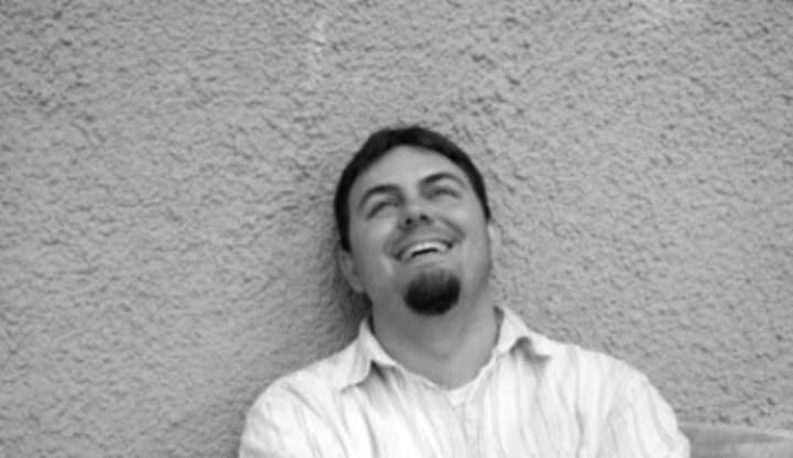 Černobílá fotografie muže, který je opřený o zeď a směje se
