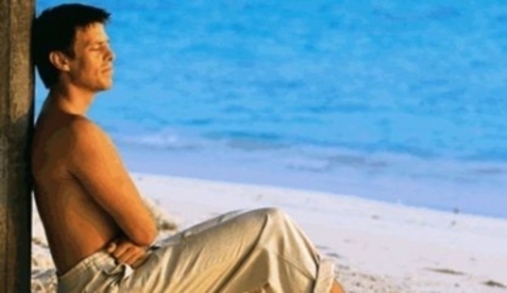 Muž sedící na pláží užívající si letní pohodu