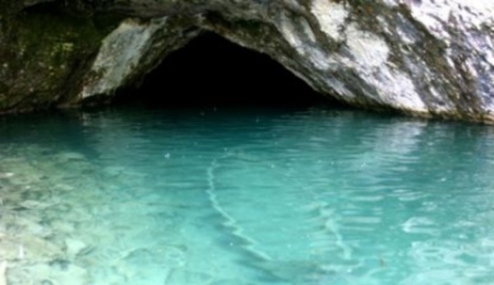 Fotografie azurového moře s potopenou loďkou před jeskyní
