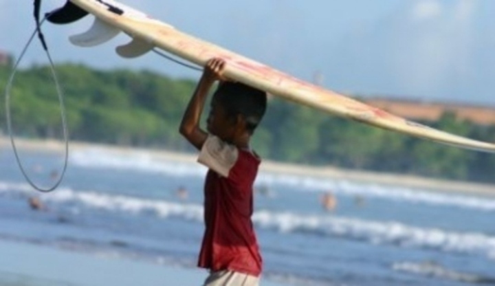 Snímek zachycující malého kluka držící surfingové prkno nad hlavou