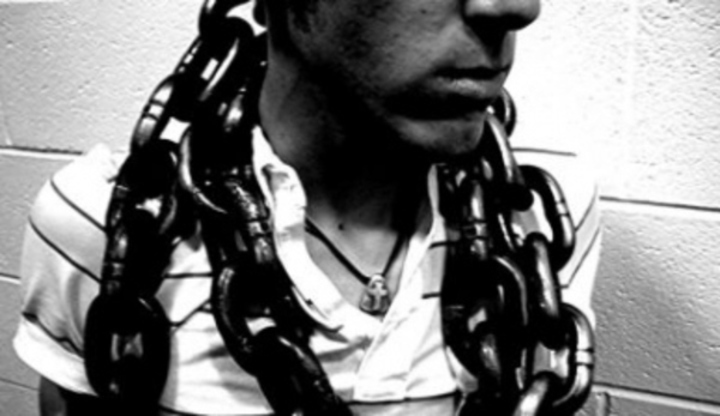 Černobílá fotografie zachycující muže, jenž má omotán kolem krku řetěz