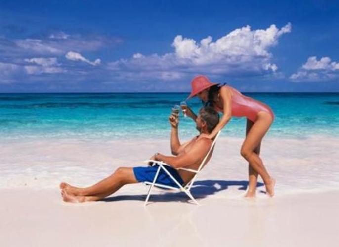Partnerská dvojice zachycena na pláži, kdy žena líbá muže sedícího na židli
