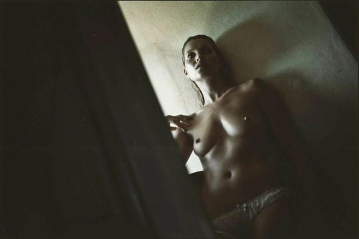 Fotografie zachycující nahou ženu opřenou o zeď