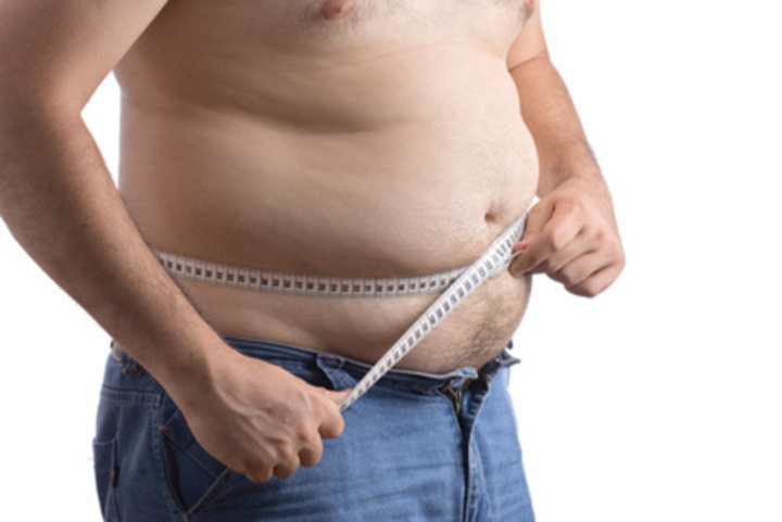 Snímek zachycující nadváhu muže, měřící si nadbytek tuku v oblasti břicha