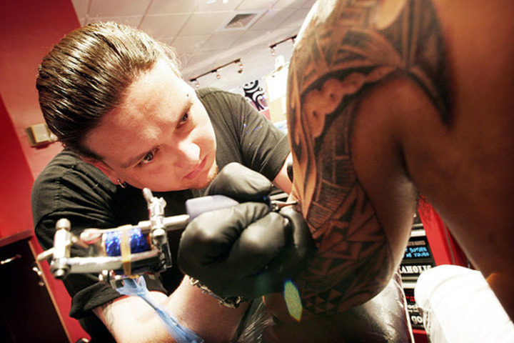 Fotografie zachycující tatéra při své práci v tetovacím salóně