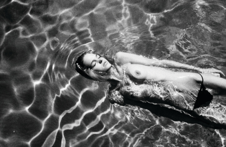 Černobílá fotografie nahé ženy ležící v bazéně