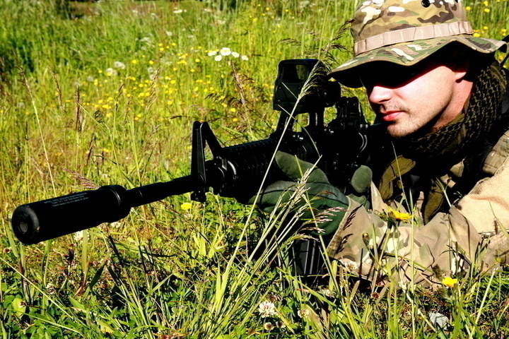 Fotografie vojáka se zbraní, který leží v trávě