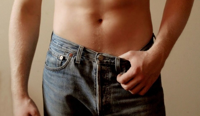 Fotografie muže s odhaleným břichem a s palcem za pasem kalhot
