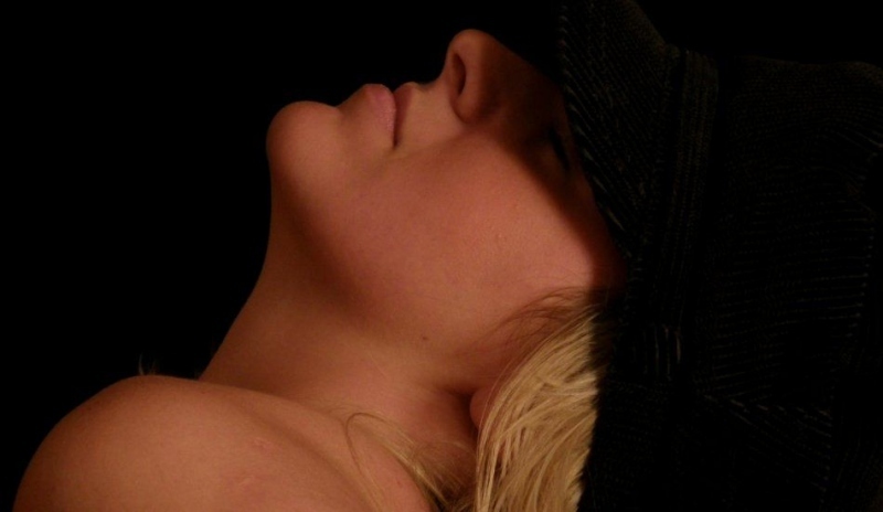 Fotografie blond ženy se zakloněnou hlavou na černém podkladu