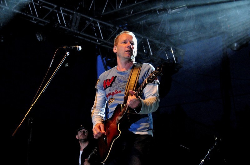Muž stojí na pódiu před mikrofonem a hraje na kytaru