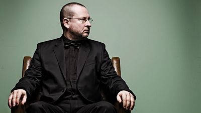 Fotografie muže sedícího na židli v černém obleku s hlavou otočenou na bok