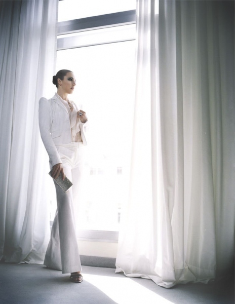 Žena v bílém kostýmu stojí u okna