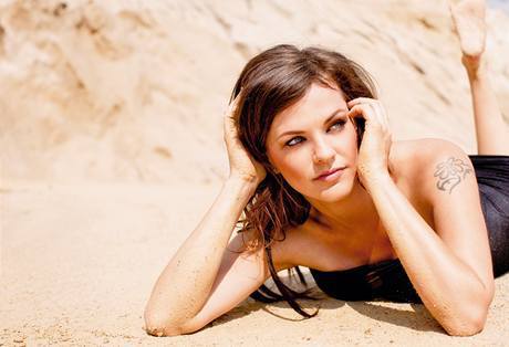 Marta Jandová leží na písku s tetováním na rameni
