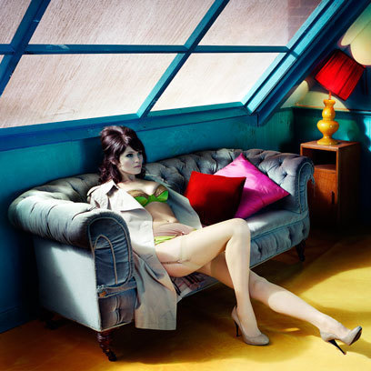 Herečka Gemma Arterton sedící na pohovce v pokoji s barevnými doplňky v plášti a ve spodním prádle