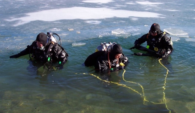 Fotografie tří potápěčů vycházejících z vody