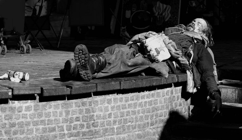 Černobílá fotografie muže bezdomovce ležícího na římse 