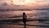 Fotografie ženy stojící na břehu moře při západu slunce