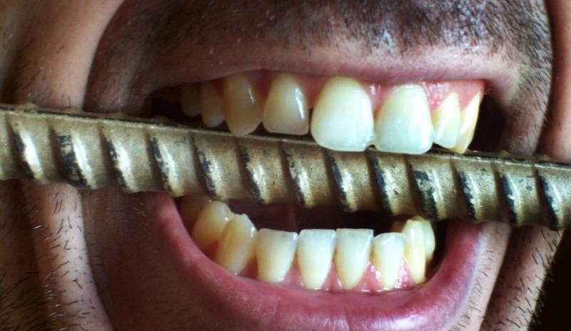 Fotografie muže držícího v zubech kovovou tyč