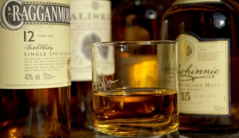 Sklenice na whisky mezi láhvemi alkoholu