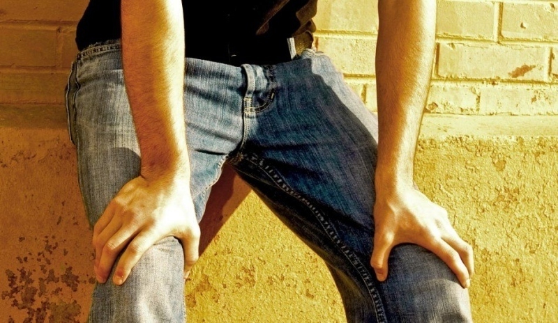 Detailní záběr na muže v džínách opřeného o zeď a kolena