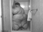 Černobílá fotografie obézního muže stojícího ve sprše