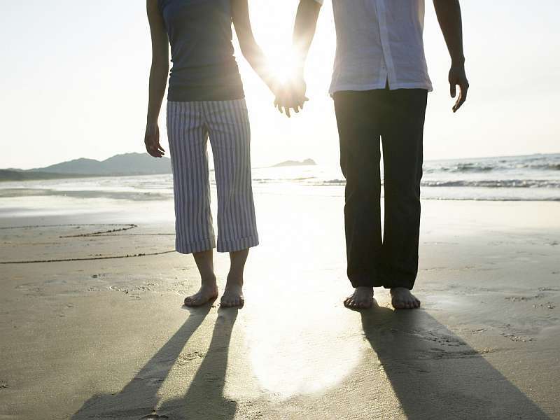 Pár držící se za ruce na pláži u moře