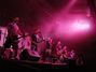 Skupina lidí na pódiu stojí ve fialovém světle