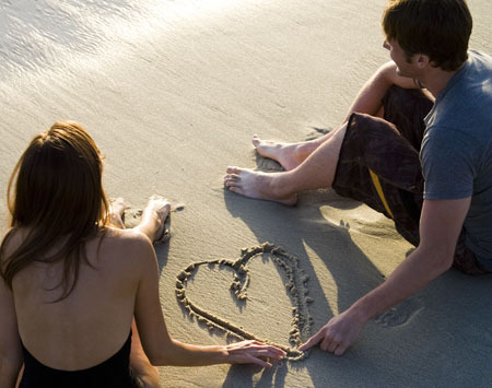 Muž se ženou kreslí srdce do písku