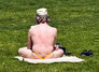 Muž otočený zády sedí v plavkách na trávě