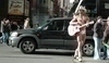 Fotografie muže ve slipech a s kytarou v ruce kráčí po ulici