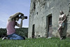 Muž s fotoaparátem fotografuje nahou ženu opírající se o zeď